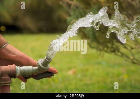 Eau s'écoulant d'un robinet extérieur en métal. Une main ferme le robinet. Banque D'Images