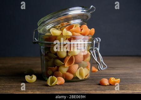 Pâtes Conchiglie colorées dans un pot en verre sur fond en bois. Vues de face, gros plan Banque D'Images