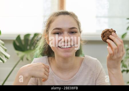 Adolescente dirige le journal de vlog culinaire pour adolescents, fille montre des muffin de chocolat fraîchement cuit, regarde la webcam, dit la recette Banque D'Images