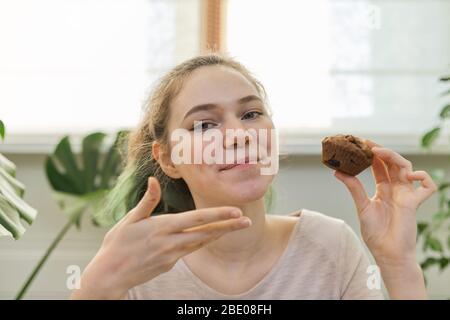 Adolescente dirige le journal de vlog culinaire pour adolescents, fille montre des muffin de chocolat fraîchement cuit, regarde la webcam, dit la recette Banque D'Images