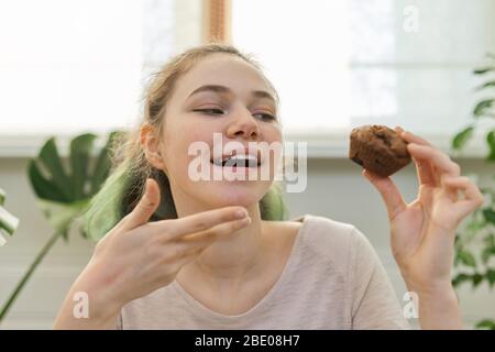 Adolescente dirige le journal de vlog culinaire pour adolescents, fille montre des muffin de chocolat fraîchement cuit, regarde la webcam, dit la recette Banque D'Images