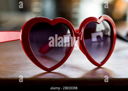 Lunettes de soleil en forme de cœur à proximité sur le bureau. Lunettes pour femme accessoire vintage. Lunettes de soleil en plastique rouge en forme de coeur. Banque D'Images