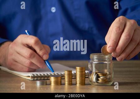 L'homme calcule les économies. Concept de planification budgétaire. Homme d'affaires travaillant au bureau. L'homme met des pièces dans le pot. Banque D'Images