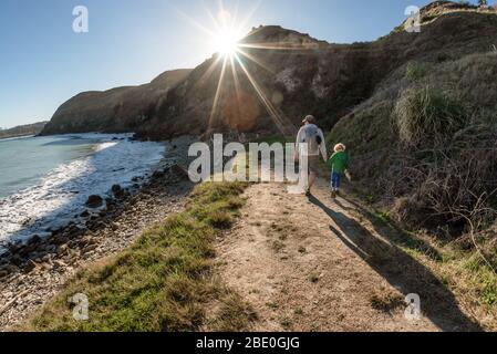 Papa et petit enfant qui se tiennent sur le chemin près de l'océan par temps ensoleillé Banque D'Images