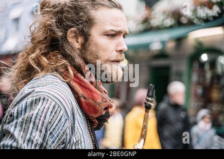 Homme blond avec cheveux longs et barbe vêtu de vêtements hippie avec saxophone au milieu de la rue Banque D'Images