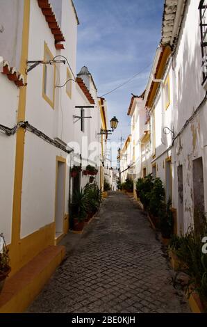 Rue pavée typique étroite de murs blancs et jaune bordant le quartier juif d'Elvas. Lampes et ciel bleu. Portugal. Banque D'Images