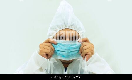 Médecin en costume blanc bioprotecteur tenant un masque bleu avec ses mains le mettant sur son visage sur fond blanc Banque D'Images