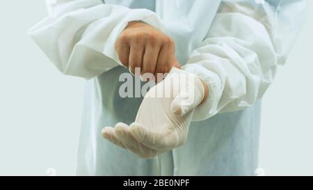 Médecin avec masque et costume blanc de bioprotection mettant des gants en latex sur les mains au premier plan sur fond blanc Banque D'Images