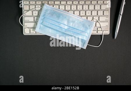 Vue de dessus de la table de bureau à la maison pendant l'éclosion de coronavirus avec clavier, masque de visage et stylo. Espace de copie. Travaillez à distance ou travaillez à domicile. Banque D'Images