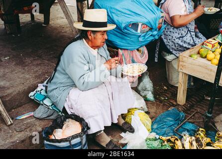 Pisac, Pérou - 29 juillet 2010: Femme âgée locale manger des nouilles sur un marché indien au Pérou portant une chapeau de paille. Banque D'Images