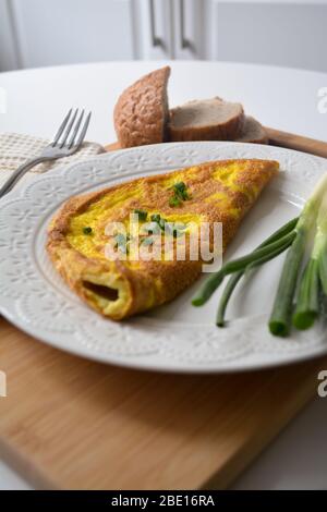 Omelette douce pour le petit déjeuner avec oignons verts de printemps et pain grillé frais sur une surface en bois avec une serviette et une fourchette en métal Banque D'Images