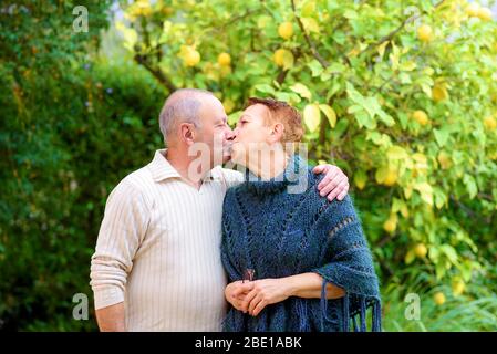 Portrait de heureux couple senior embrassant dans le jardin extérieur. Homme âgé et femme se détendant au parc le jour ensoleillé. Un couple romantique affectueux embrasse en été près de l'arbre de citron pendant le coucher du soleil . Banque D'Images