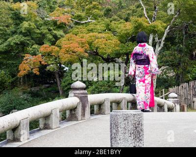 Kyoto, Japon - 30 septembre 2015 : une fille de kimono coloré se tenant sur un pont en pierre du parc Maruyama Banque D'Images