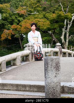 Kyoto, Japon - 30 septembre 2015 : jeune fille dans de beaux kimono assis sur un pont en pierre dans un jardin japonais traditionnel Banque D'Images