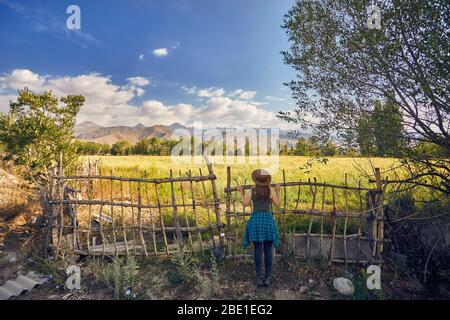 Femme au chapeau et chemise à carreaux vert près de la clôture barrière à la recherche sur le terrain dans le domaine agricole de la matinée Banque D'Images