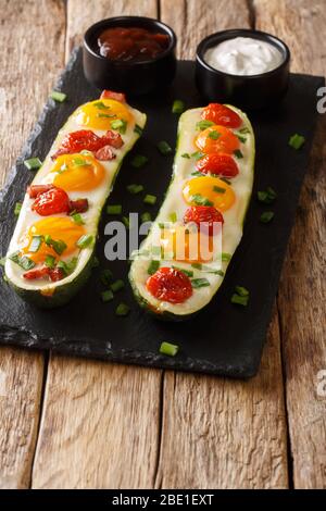 Les moitiés de courgettes cuites avec des œufs, des tomates se rapprochées sur une planche en ardoise sur la table. Verticale Banque D'Images