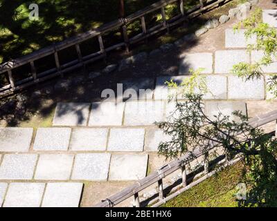 Allée de pierre baignée de soleil dans un jardin japonais serein avec clôture en bambou Banque D'Images