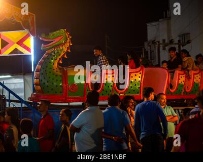 Mumbai, Inde - 01 décembre 2019: Famille indienne profitant d'une palpitante promenade en montagnes russes dans le parc d'attractions illuminé la nuit Banque D'Images