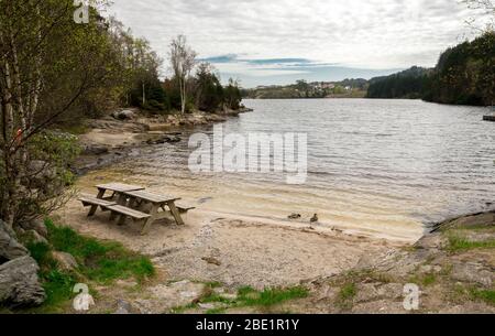 Une table de pique-nique avec bancs sur une petite plage de sable du lac Eivindsvannet à Djupadalen zone de loisirs publique, Haugesund, Norvège, mai 2018 Banque D'Images