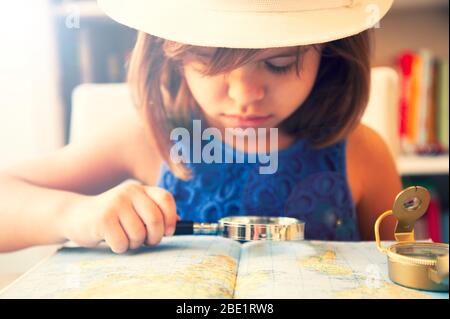 Petite fille tendance en été décontracté et chapeau blanc, regardant la carte du monde avec loupe et compas. Planification d'un voyage. Découverte du wor Banque D'Images