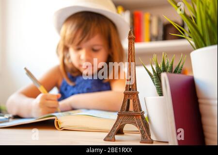 Petite fille tendance en été décontracté et chapeau blanc, fait des devoirs ou écrit des notes sur la carte. En premier plan un souvenir métallique de la tour Eiffel, su