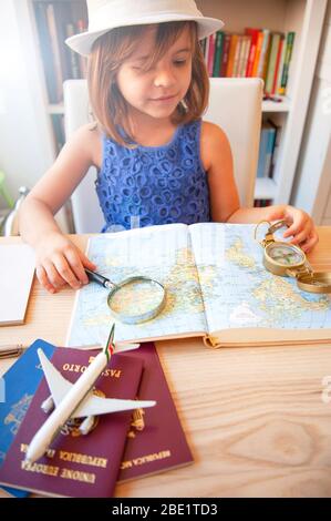 Petite fille tendance en été décontracté et chapeau blanc, regardant la carte du monde avec loupe et compas. Planification d'un voyage en famille. Passeport Banque D'Images