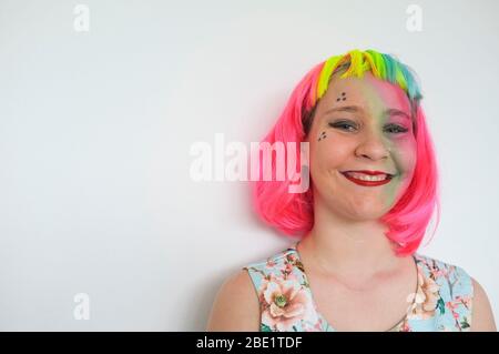 Une adolescente avec une perruque multicolore et un lourd appoint contre un mur blanc. Banque D'Images