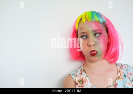 Une adolescente avec une perruque multicolore et un lourd appoint contre un mur blanc. Banque D'Images