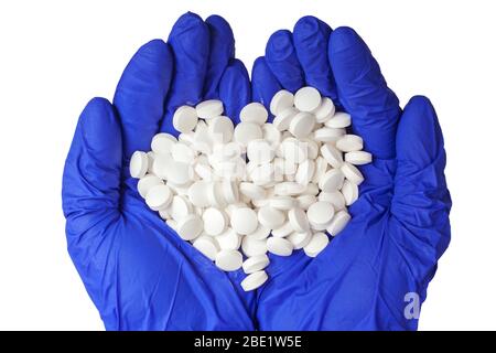 Les mains dans les gants médicaux contiennent une poignée de pilules blanches. Gants jetables bleus isolés sur un fond blanc. Le concept pharmaceutique. Le médicament Banque D'Images