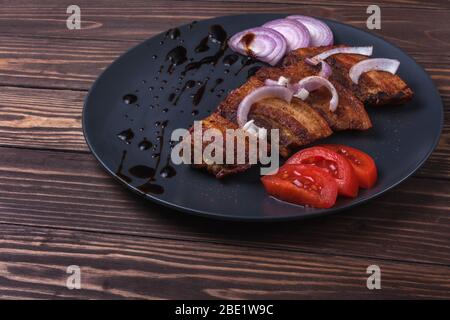 Ventre de porc frit avec sauce et oignons dans une plaque gris foncé sur un plan d'examen en bois Banque D'Images
