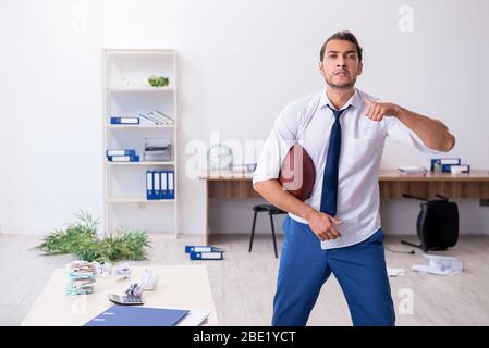 Jeune employé jetant du ballon de rugby dans le bureau Banque D'Images