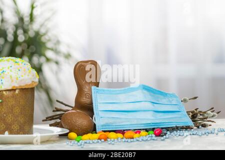 Gâteau de Pâques, masque de protection médical et œufs au chocolat et lapin, gros plan. Protection contre les virus. Le concept de la célébration du Saint Banque D'Images