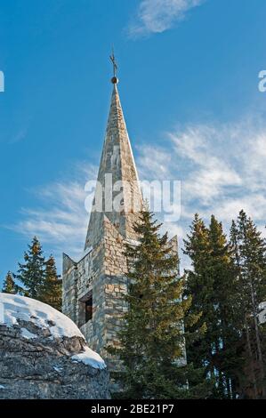 Haut d'une église en pierre steeple avec croix dans les arbres contre fond bleu ciel Banque D'Images