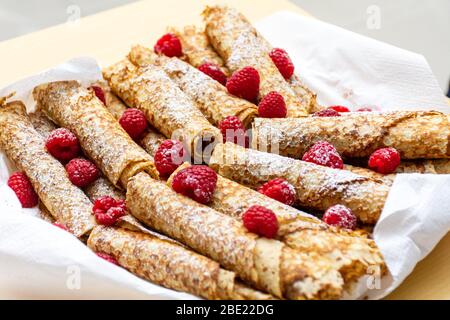 Pile faite maison de crêpes françaises laminées avec des framboises en poudre de sucre (givrage) conçues sur une assiette pour le petit déjeuner ou un en-cas. Banque D'Images