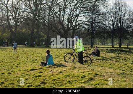 Un policier sur un vélo demande à une fille de se déplacer pour enfreindre les règles de verrouillage sur Clapham Common à Londres pour réduire l'épandage de Coronavirus Covid-19 Banque D'Images