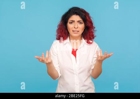 Que voulez-vous ? Portrait d'une femme hipster agacée avec des cheveux rouges fantaisie debout avec des mains levées, gestionnant en perplexité regardant irritant indigné Banque D'Images