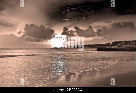 Lever du soleil, à Swanage Dorset en monotone noir et blanc, avec des nuages cumulés, et bout de champ au loin, une mer calme Banque D'Images