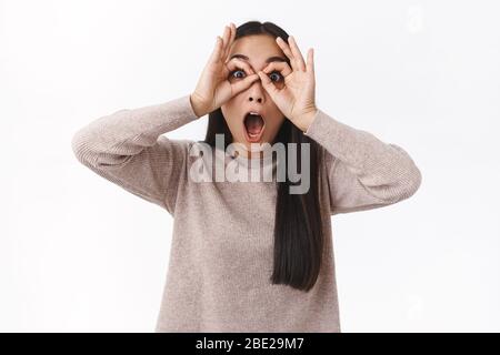 Surprise, impressionnée et sans voix jeune fille asiatique avec un méroiazé et excité, faire des lunettes de doigts et des yeux craptés appareil-photo, check-out génial Banque D'Images