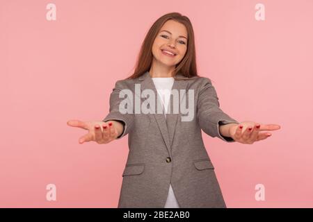 Ravi de vous rencontrer ! Portrait de la jeune femme sympathique en costume d'affaires soulevant les mains large ouvert donnant des chopes libres, geste de générosité, hôtesse accueillant avec s Banque D'Images