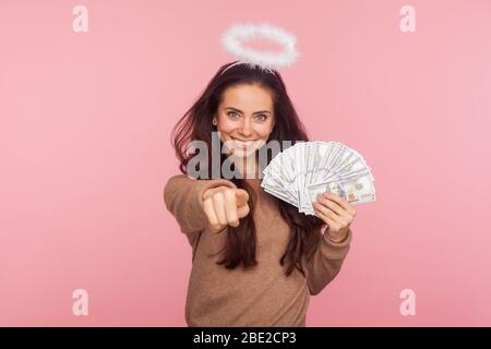Portrait de heureuse jeune femme angélique avec halo au-dessus de la tête tenant des billets en dollars et pointant vers la caméra, choisir le gagnant de loterie, encourageant à ea Banque D'Images