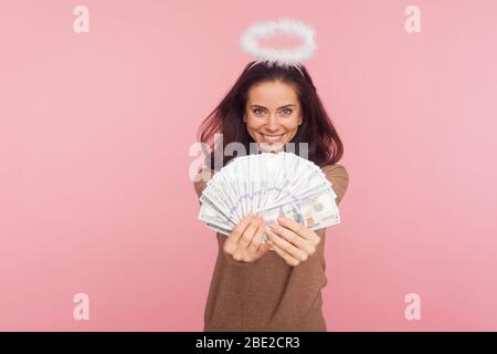 Portrait de heureuse jeune femme angélique avec halo au-dessus de la tête tenant des billets en dollars, montrant de l'argent et se vantant gagner de loterie, riche vie paradisiaque. i Banque D'Images