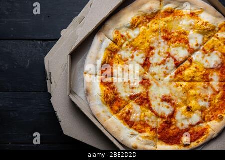 Pizza margherita dans une boîte de livraison ouverte, image à faible clé. Livraison des aliments, concept de nourriture à emporter: Pile de boîtes à pizza sur fond de bois noir Banque D'Images