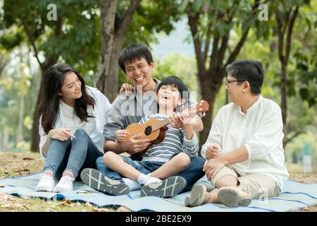 Bonne famille avec grand-mère, maman avec papa enseignant le fils jouant de la guitare et chanter une chanson dans le parc, profiter et se détendre les gens pique-nique dehors Banque D'Images