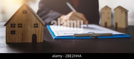 immobilier, propriété et propriétaire de maison signe le concept de contrat, petit modèle de maison en bois sur table de bureau avec main de l'acheteur de femme signe sur l'accord de location Banque D'Images