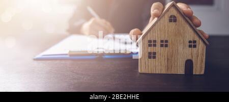 immobilier, propriété et propriétaire de maison signe le concept de contrat, petit modèle de maison en bois sur table de bureau avec main de l'acheteur de femme signe sur l'accord de location Banque D'Images