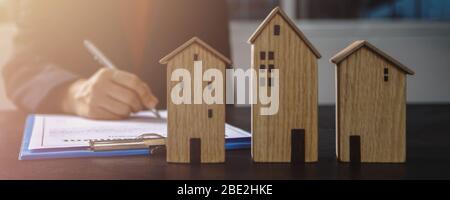 immobilier, propriété et propriétaire de maison signe le concept de contrat, petit modèle de maison en bois sur table de bureau avec main de l'acheteur de femme signe sur l'accord de location Banque D'Images