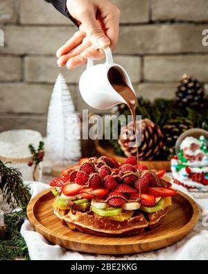 homme qui verse du chocolat sur la gaufres avec des tranches de fruits Banque D'Images