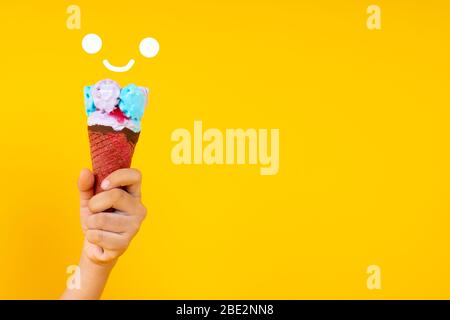 Gros plan tenant main cône coloré de crème glacée sur fond jaune avec espace de copie Banque D'Images