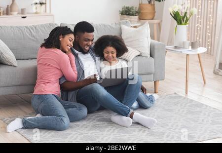 Papa noir, maman, et petite fille utilisant l'ordinateur portable à la maison ensemble Banque D'Images