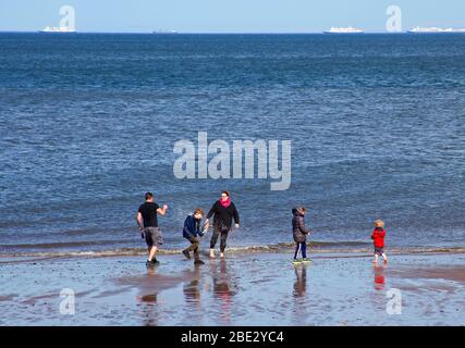 Portobello Promenade, Édimbourg, Écosse, Royaume-Uni. 11 avril 2020. Température de 16 degrés avec plein soleil dans l'après-midi après un début nuageux. Le samedi de Pâques, une plage très calme le troisième week-end de coronavirus Lockdown. Une famille s'amuse au bord de la mer. Banque D'Images